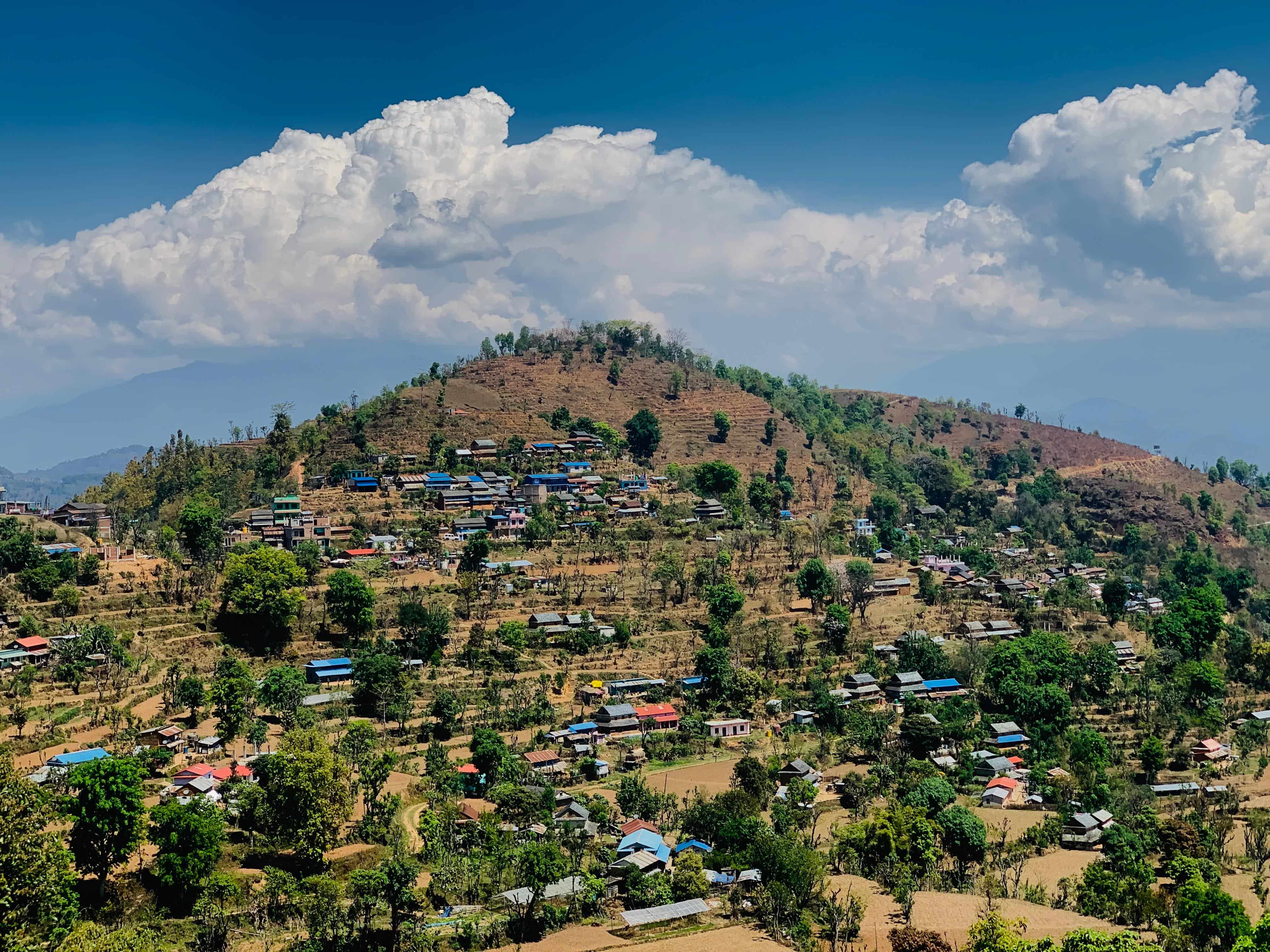 Scenic view of Khirre Village in Siddhalek Rural Municipality, featuring hillside settlements, agricultural fields, lush greenery, and dramatic clouds.